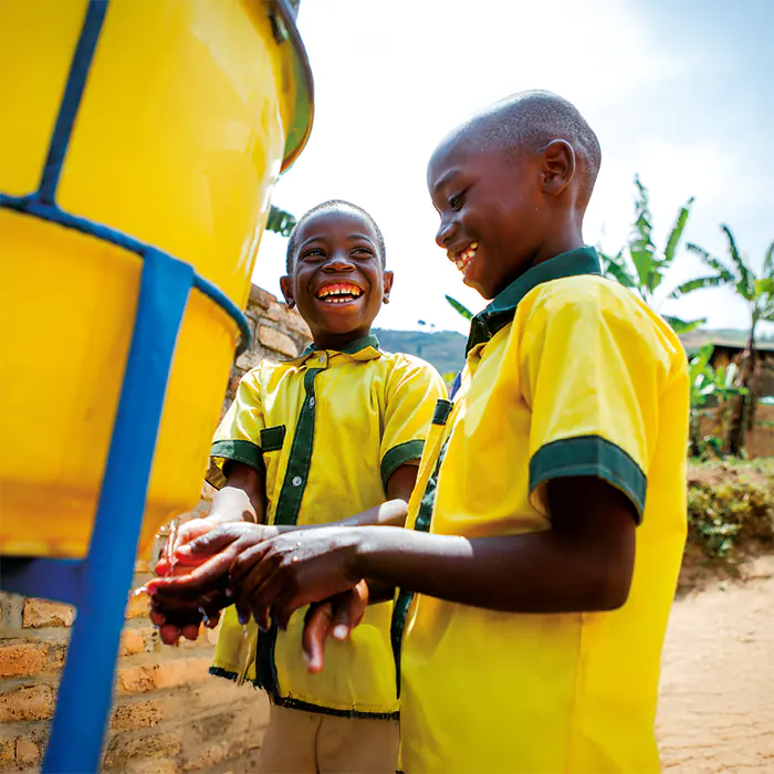 Two smiling african boys drink water from a tap at school