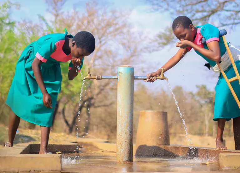 2 schoolgirls drinking water out of taps, Malawi