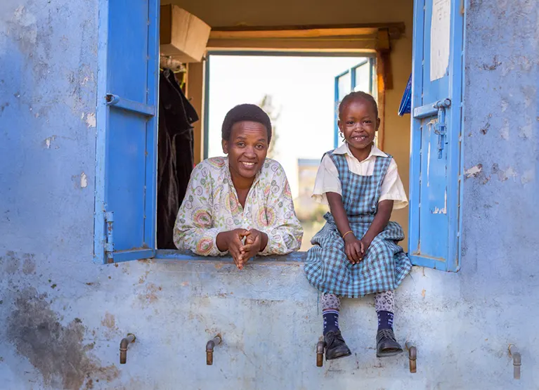 Water vendor and her daughter smile leaning out of their kiosk in Naivasha, Kenya